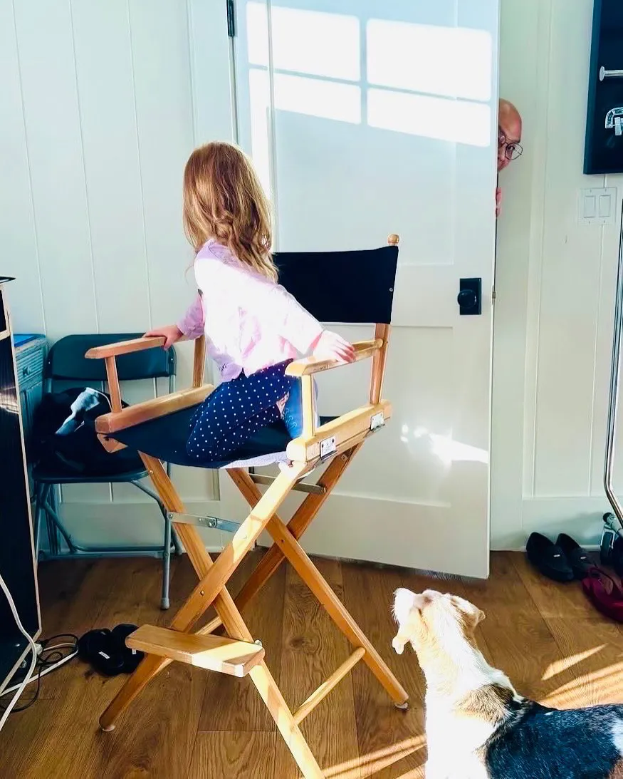 Princess Lilibet sitting in a directors chair turning to look at Daniel Martin peeking from a doorway