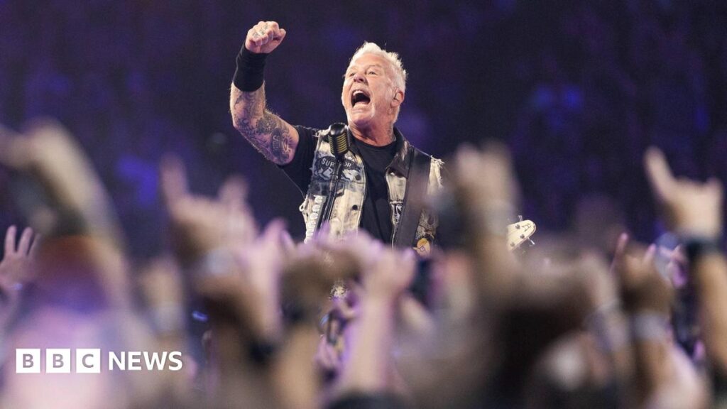 Metallica teams up with Welsh Blood Service ahead of Cardiff show Lead singer and guitarist of Metallica, James Hetfield performs onstage at Lumen Field. He's surrounded by a crowd of people with their arms up. He's wearing a black t shirt, arm cuff and a denim vest. He's holding a guitar. He's got his arm up in the air and appears to be shouting.