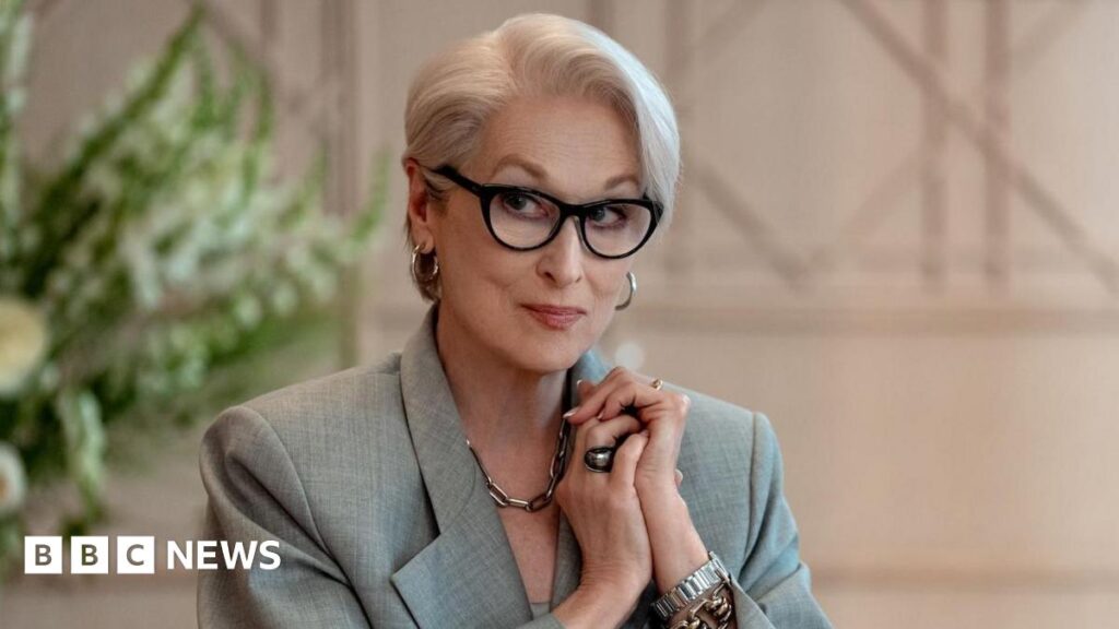 Image of Meryl Streep in a still from The Devil Wears Prada 2. She is wearing a grey blazer, assorted jewellery and black glasses.