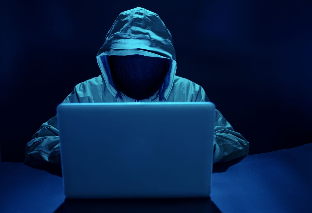 Unidentifiable person in hoodie hunched over laptop