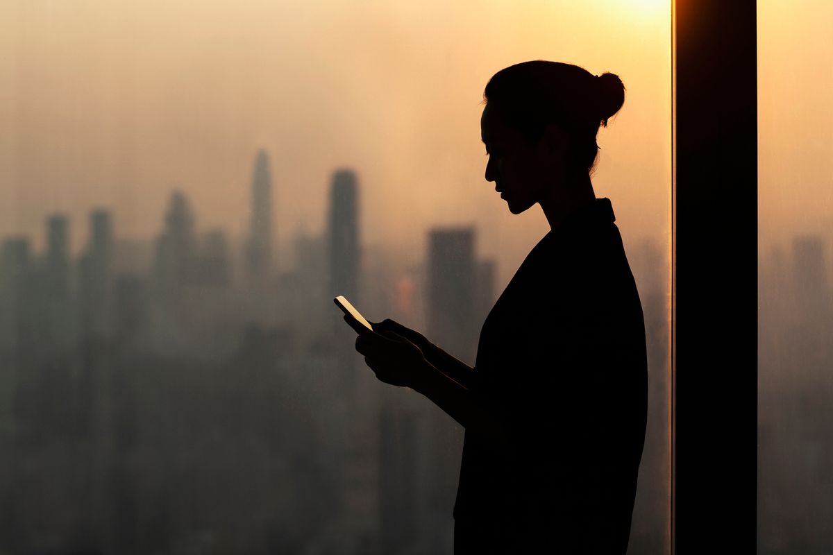 Silhouette of a young woman using a smartphone next to a window