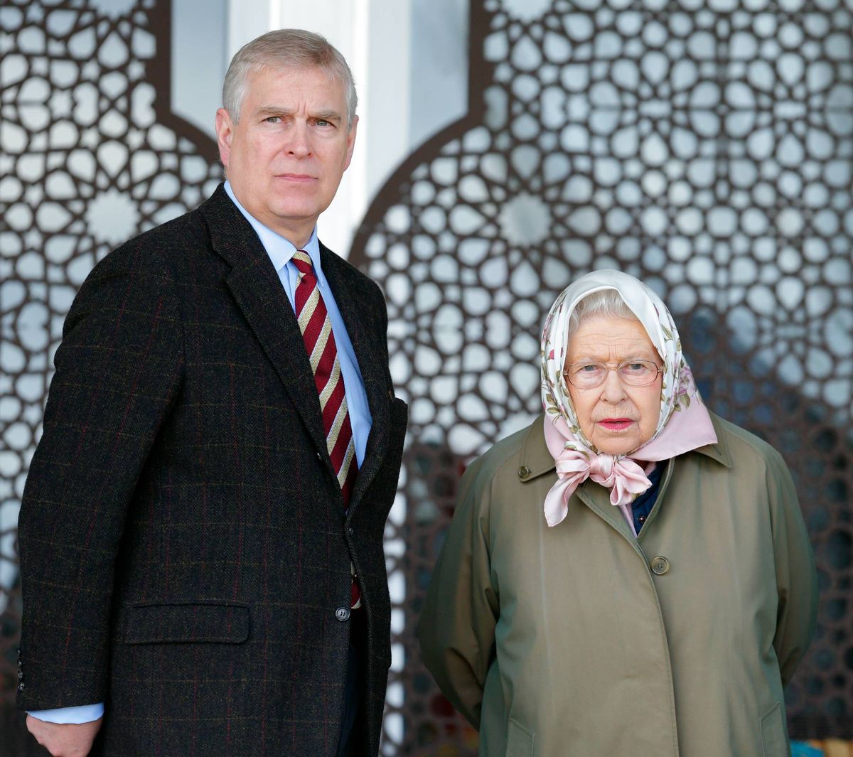 An adult male in formal attire and an adult female with a headscarf stand side by side in front of a patterned wall.