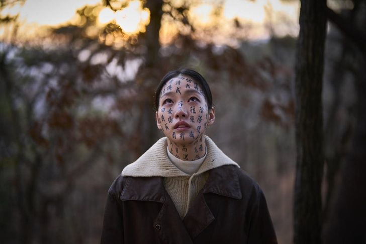 Lee Hwa-rim, played by Kim Go-eun, has the words to a Buddhist sutra written on her face in a scene from the movie 'Exhuma.' Courtesy of Showbox