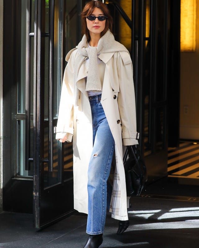 Individual exiting a building in a light trench coat and denim.