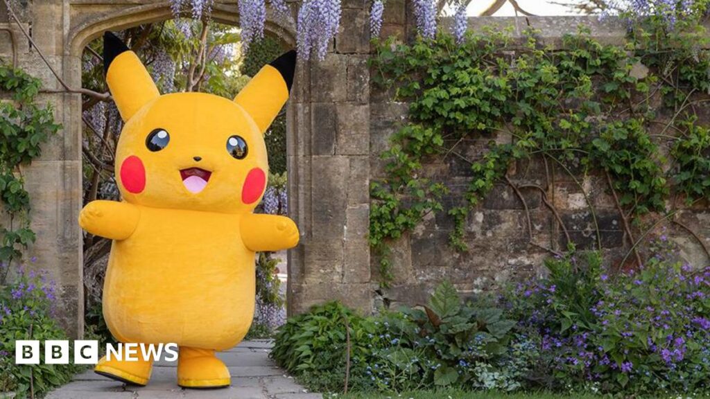 Pokemon Mega Evolution trails to launch at National Trust sites Pokemon character Pikachu standing in a stone doorway in a garden with an abundance of flowers owned by the National Trust on a sunny day.