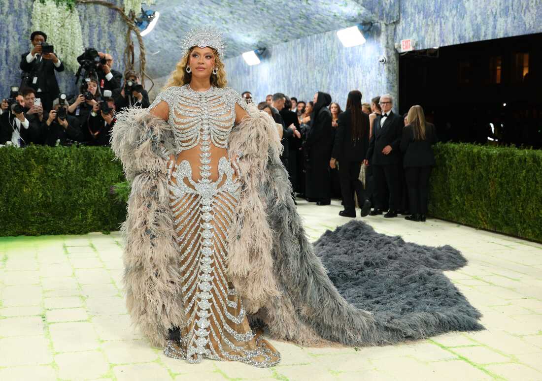 Beyoncé arrives for the 2026 Met Gala. She is wearing a sheer gown adorned with silver that looks like a ribcage, pelvis and vertebrae. She has silver headpiece and a gray train.