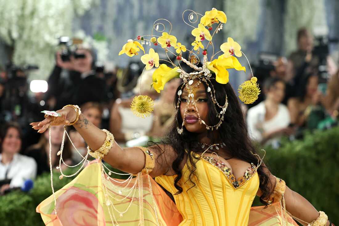 SZA attends the 2026 Met Gala. She is wearing a yellow gown and a headpiece that has orchids and shells woven together.