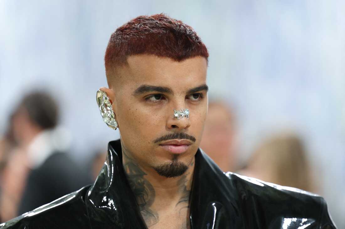 Singer Rauw Alejandro attends the 2026 Met Gala. He is wearing a silver piece that covers most of his ear and jewelry that goes across his nose.