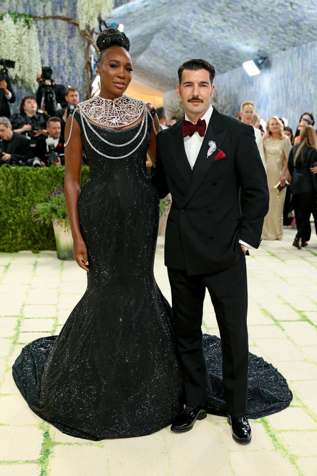 Co-chair Venus Williams arrives with her husband Andrea Preti. She is wearing a black sequin floor-length gown and a metallic neckpiece. He is wearing a black suit with a maroon bowtie. 