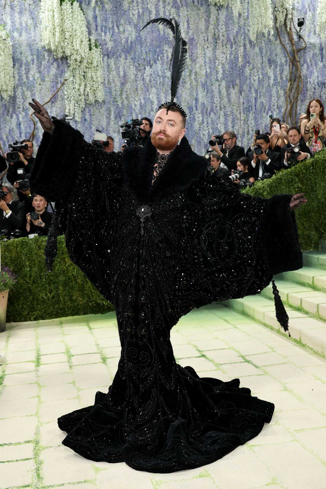Sam Smith attends the 2026 Met Gala. They are wearing a black sequined gown with feather headpiece.
