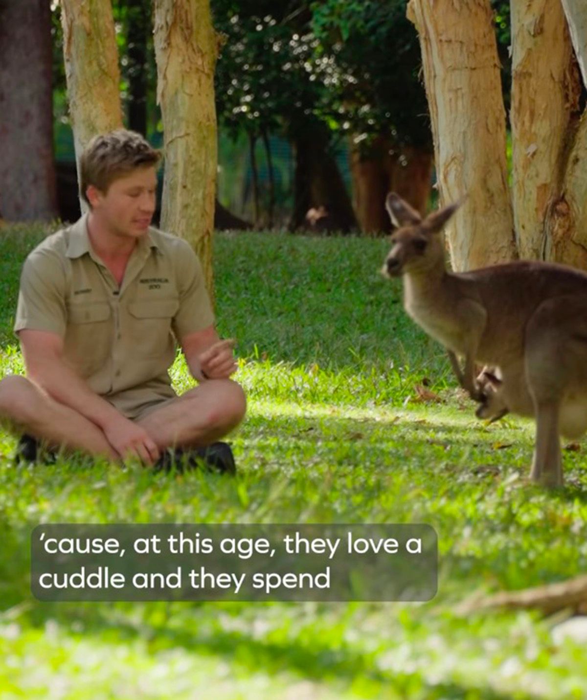 A photo of Robert Irwin sitting on the ground surrounded by kangaroos