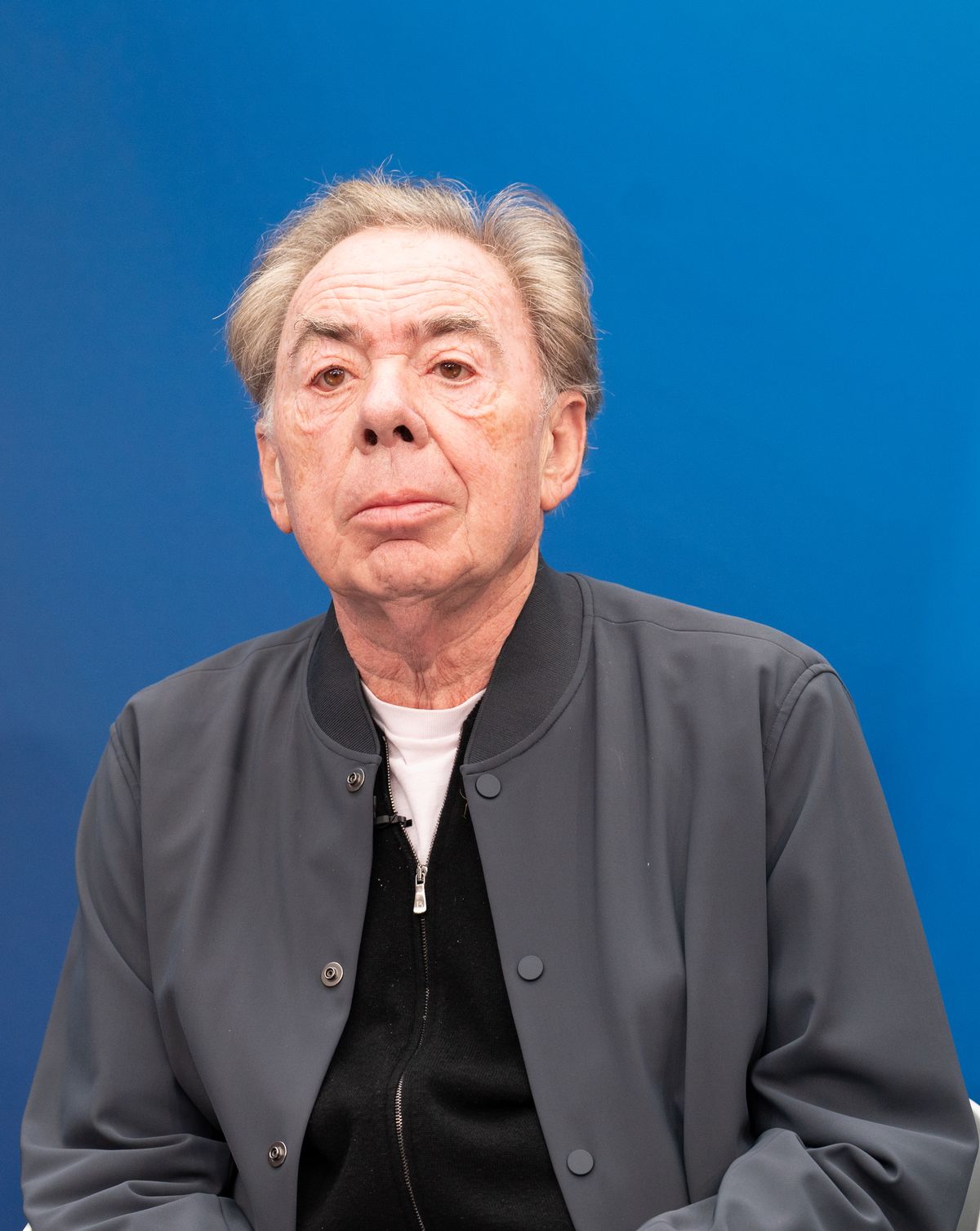 Andrew Lloyd Webber in grey cardigan against a blue backdrop