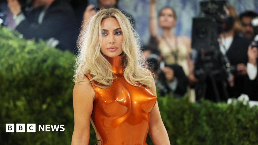 Kim Kardashian with long, blonde hair, wearing a metallic orange breastplate as she poses at the Met Gala.
