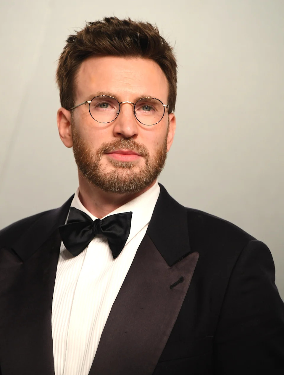 Person in a formal suit and bow tie, wearing round glasses, looking ahead with a neutral expression
