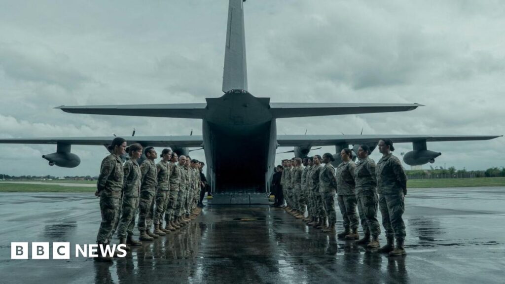 RAF Mildenhall crews praised for role in new Jack Ryan film Military personnel form two lines, facing each other, to the rear of a military aircraft which has its ramp down at the bottom. It is a grey and wet day. The servicemen and women have their hands placed behind their backs.