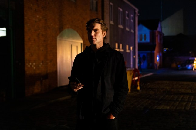 Theo Silverton holding a phone in Coronation Street