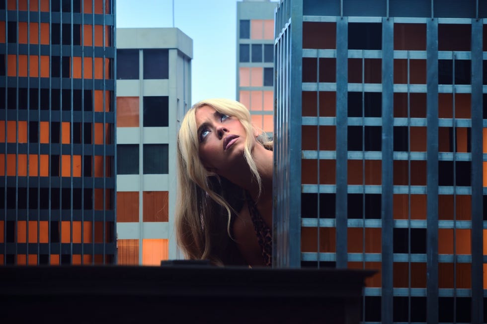 a woman peering over buildings in an urban setting