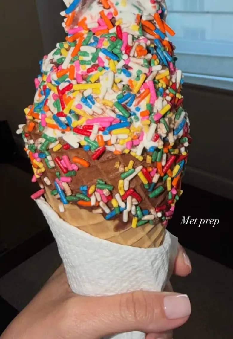 Ice cream cone with chocolate and vanilla swirls topped with colorful sprinkles, held in a napkin