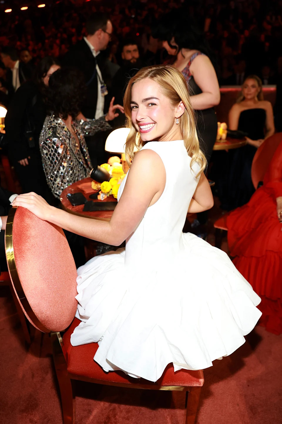 Person in a ruffled, white dress smiles back at the camera while seated at an event