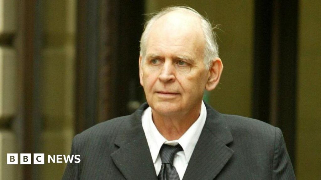 Tam Paton leaving court in 2006. He has white hair and is wearing a black suit and tie over a white shirt.