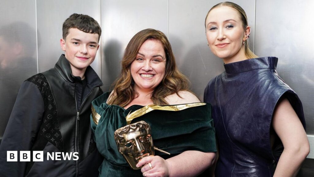 Owen Cooper and Erin Doherty standing either side of a grinning Jessica Gunning, who's holding her Bafta mask trophy