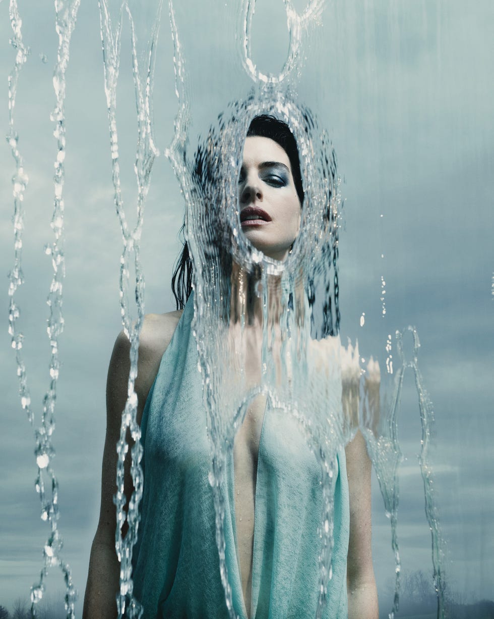 A person partially obscured by flowing water, set against a cloudy sky.