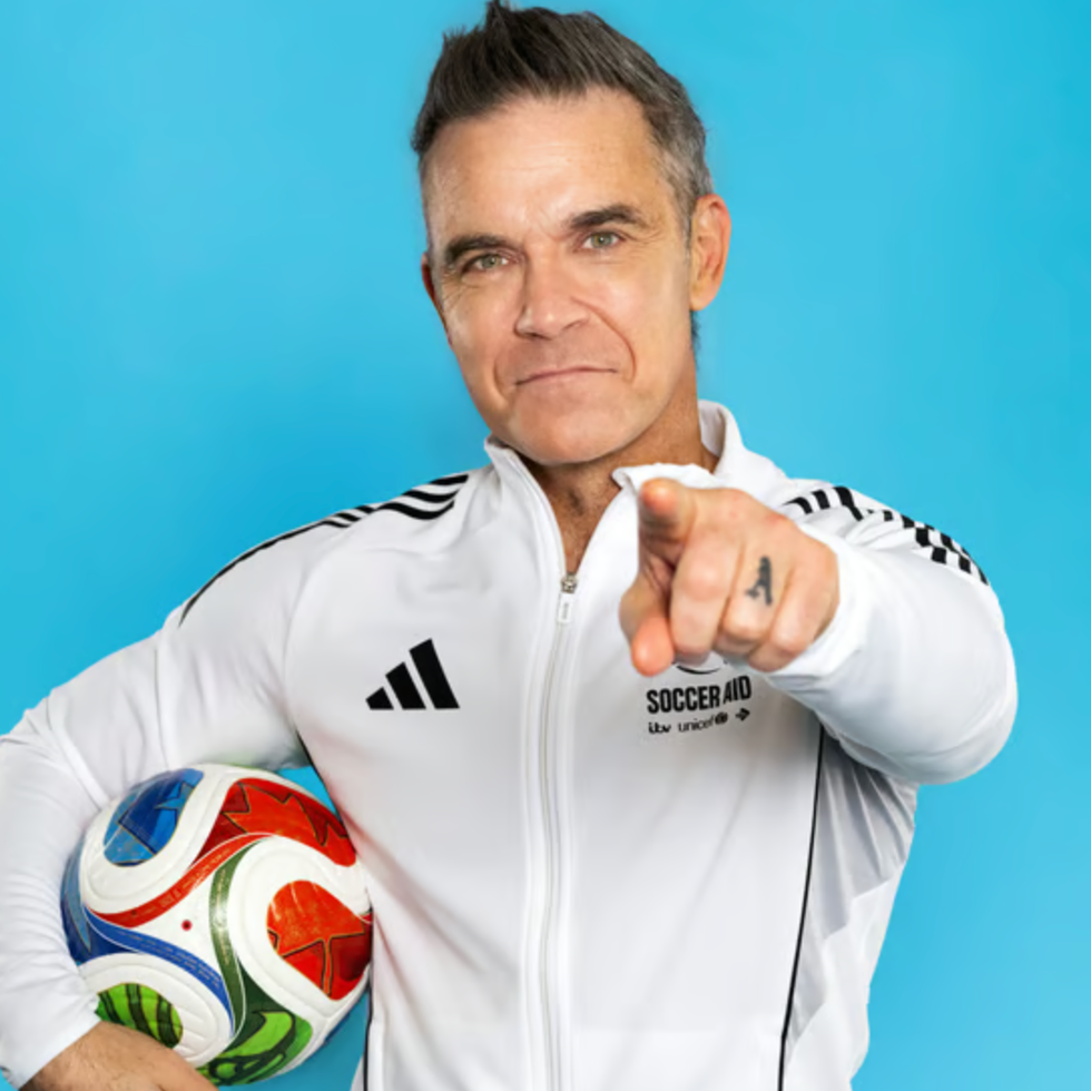 Soccer aid line up a person in a white athletic jacket holding a soccer ball and pointing