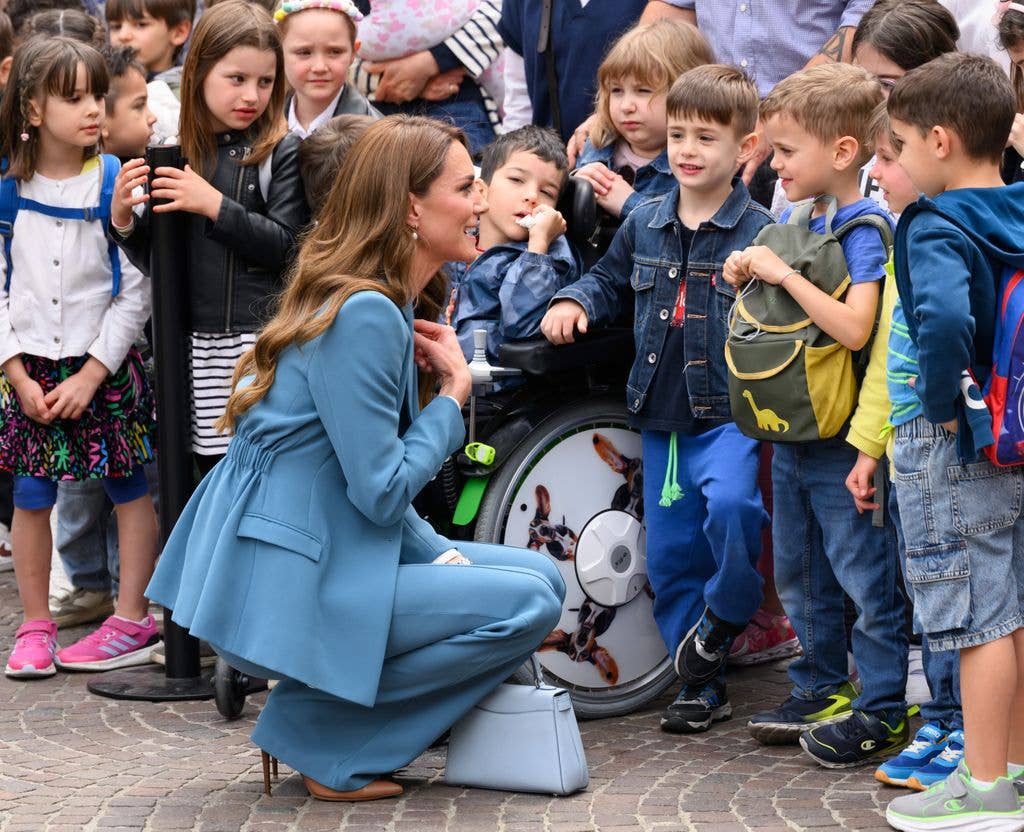 Princess Kate in blue suit bending down in front of children 