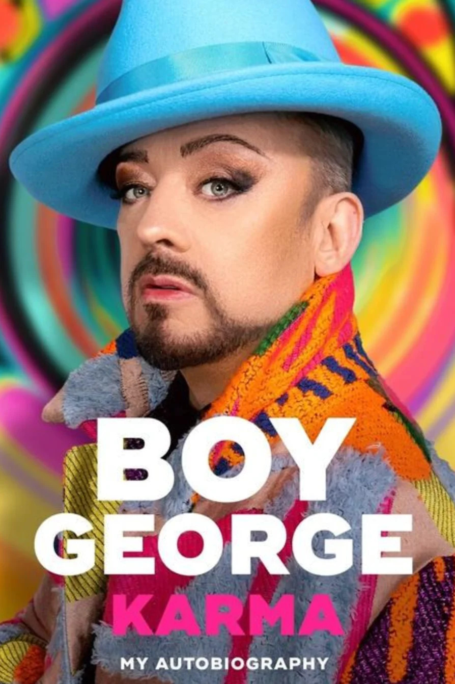 Boy George in a vibrant, patterned outfit and hat, on the cover of "Karma: My Autobiography."