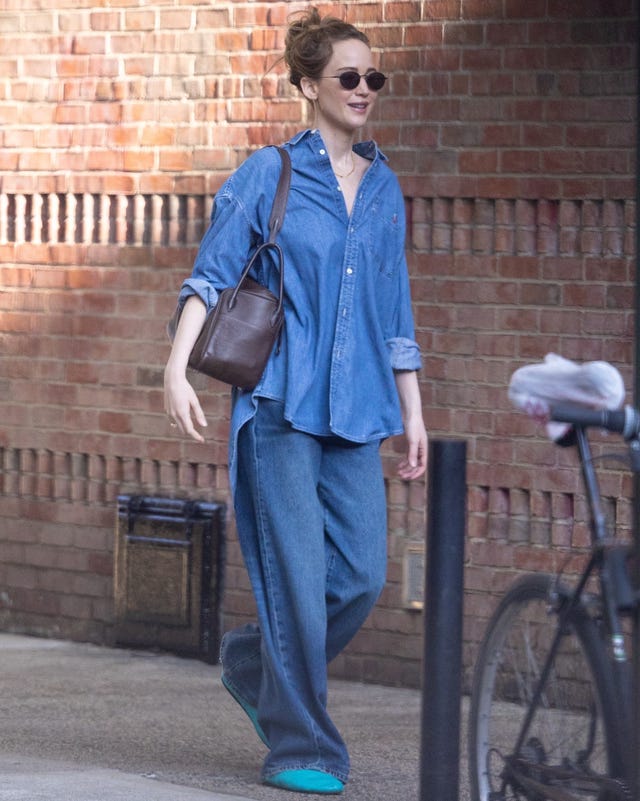 Individual walking down a street with denim attire and a handbag.