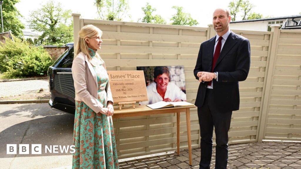 A woman with blonde hair wearing a long dress and light jacket stands near the prince who is wearing a suit and red tie and talking. Between them is a photo of a young man. There is also a gold plaque which says James' Place.