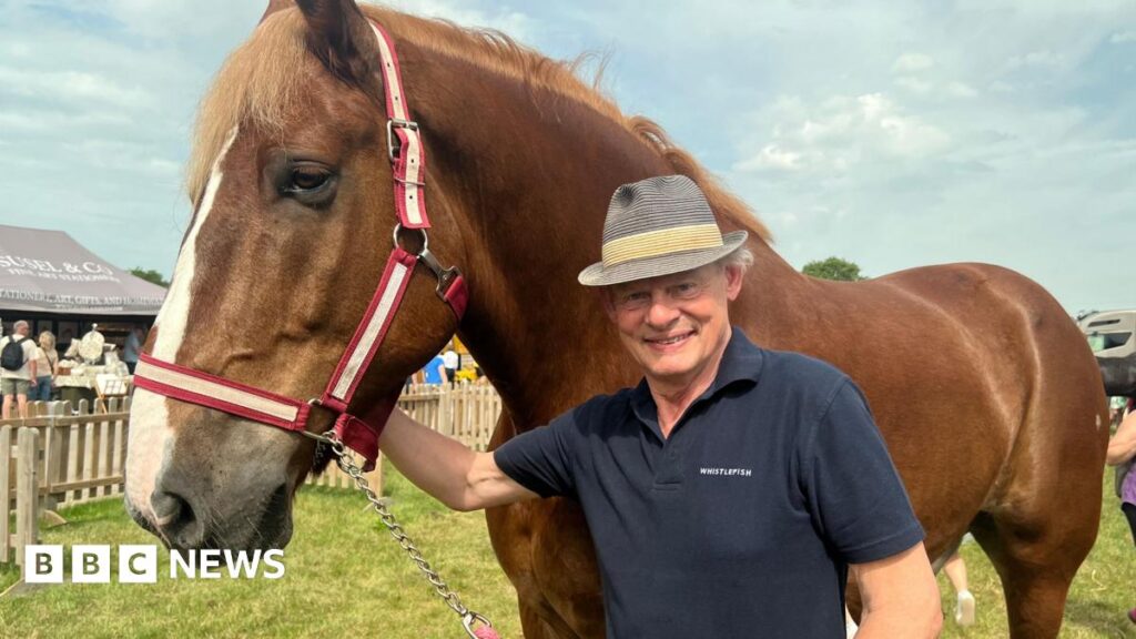 Martin Clunes shows off heavy horse at Royal Bath and West Show Martin Clunes is standing next to a horse wearing a hat and T-shirt.