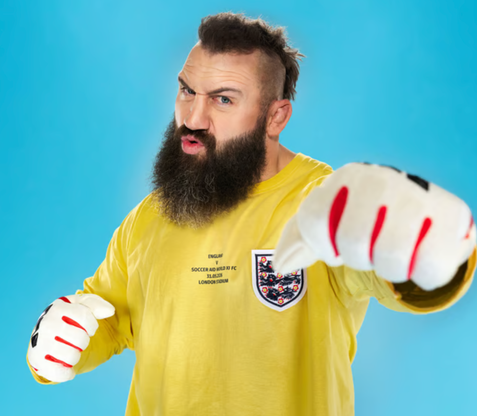 Soccer aid lineup individual wearing a yellow longsleeve shirt and oversized gloves posed against a blue background