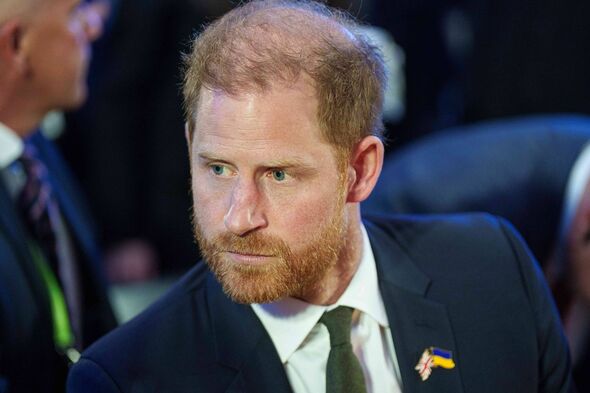 An individual with a beard and dressed in a formal suit and tie is seated and appears to be engaged in conversation. The backgro