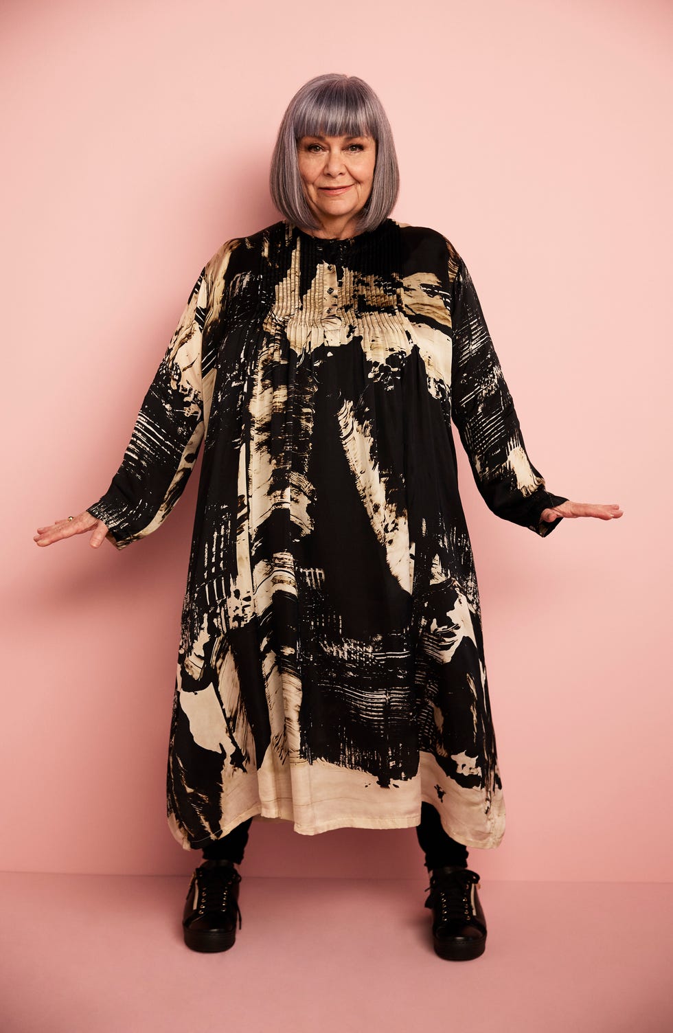 a person wearing a black and beige patterned oversized dress against a pink background