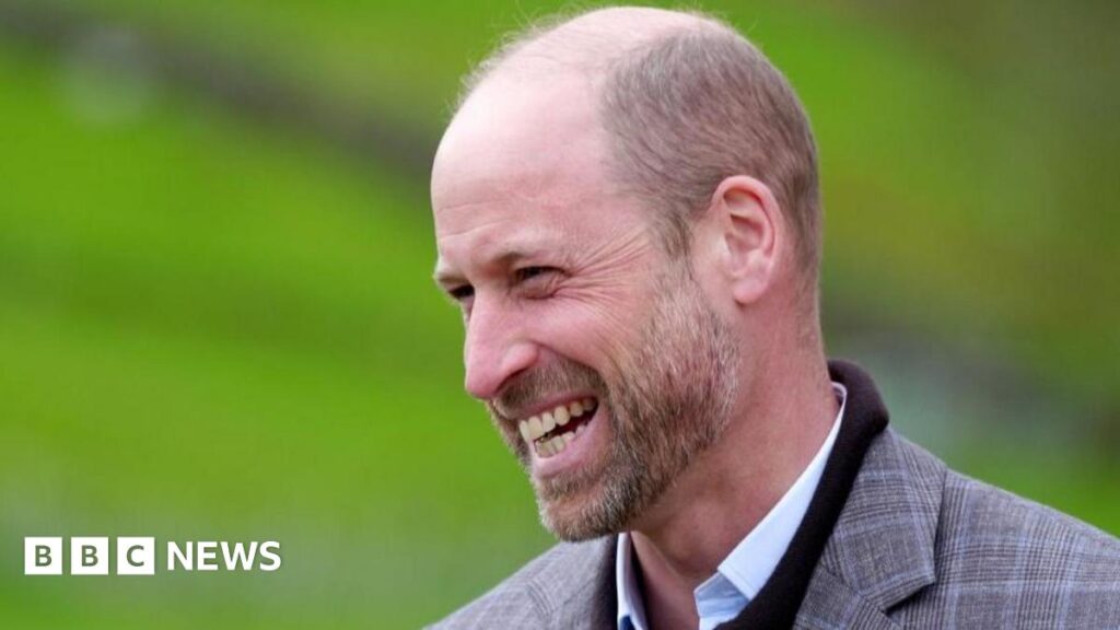 Prince William selling 20% of duchy property for housing and nature projects Prince William smiling. He is dressed in a tweed jacket worn over a dark jumper and light blue shirt.