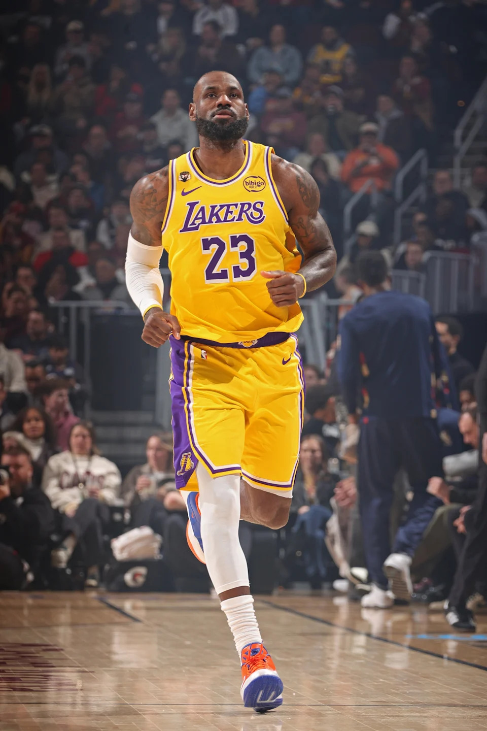 Basketball player in Lakers uniform mid-game on court, focused expression, crowded audience in background