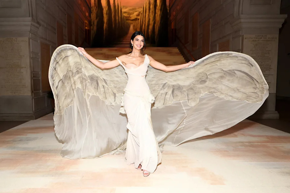 Woman on runway in flowing gown with dramatic train, smiling and holding up the sides