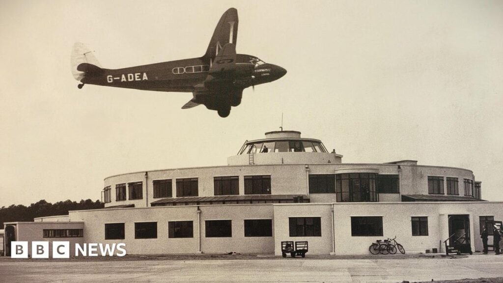 A sepia image of a circular building with a plane flying over the top of it.