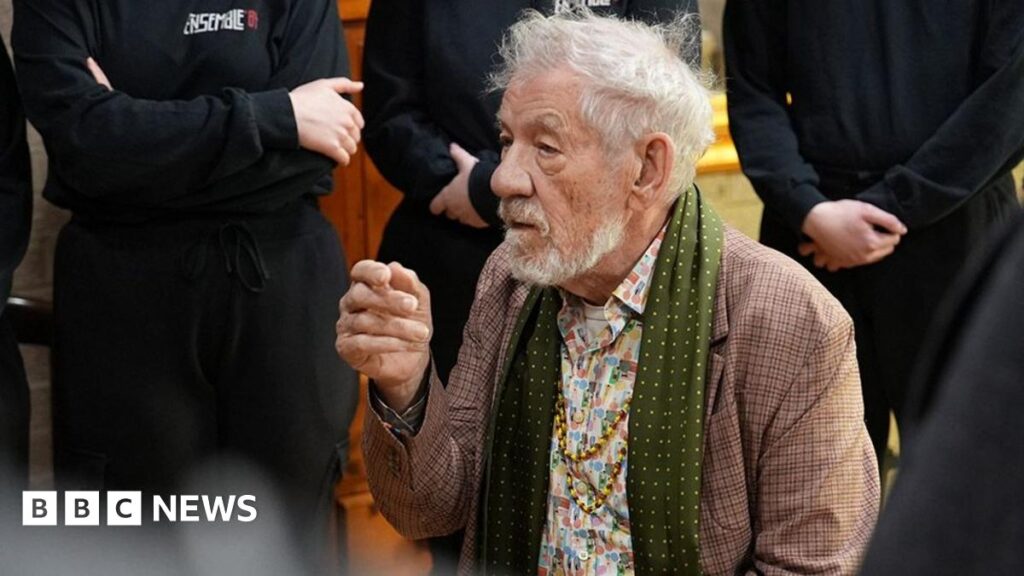 McKellen says Horden’s Ensemble 84 is bringing change and renewal Sir Ian McKellen is an 86-year-old man wearing a tweed jacket, a green silk scarf and a flowery shirt with two long gold necklaces. He is seated and behind him are a number of people wearing black who are standing listening although only their torsos are in shot