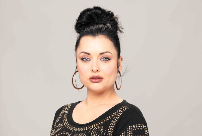 Shona McGarty poses as Whitney Dean in an EastEnders promo image wearing a black pearled top and hoop earrings.