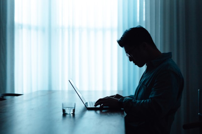 Side of Asian man in silhouette using laptop computer by the window