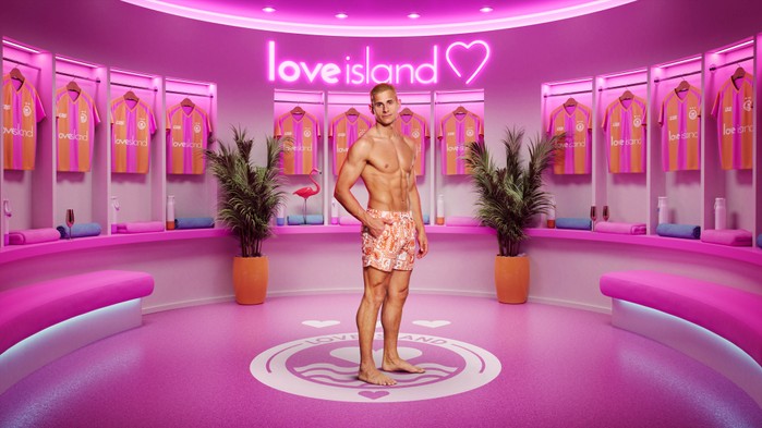 ©ITV A man stood with his body turned to the side wearing floral swim shorts with one hand in his pocket.