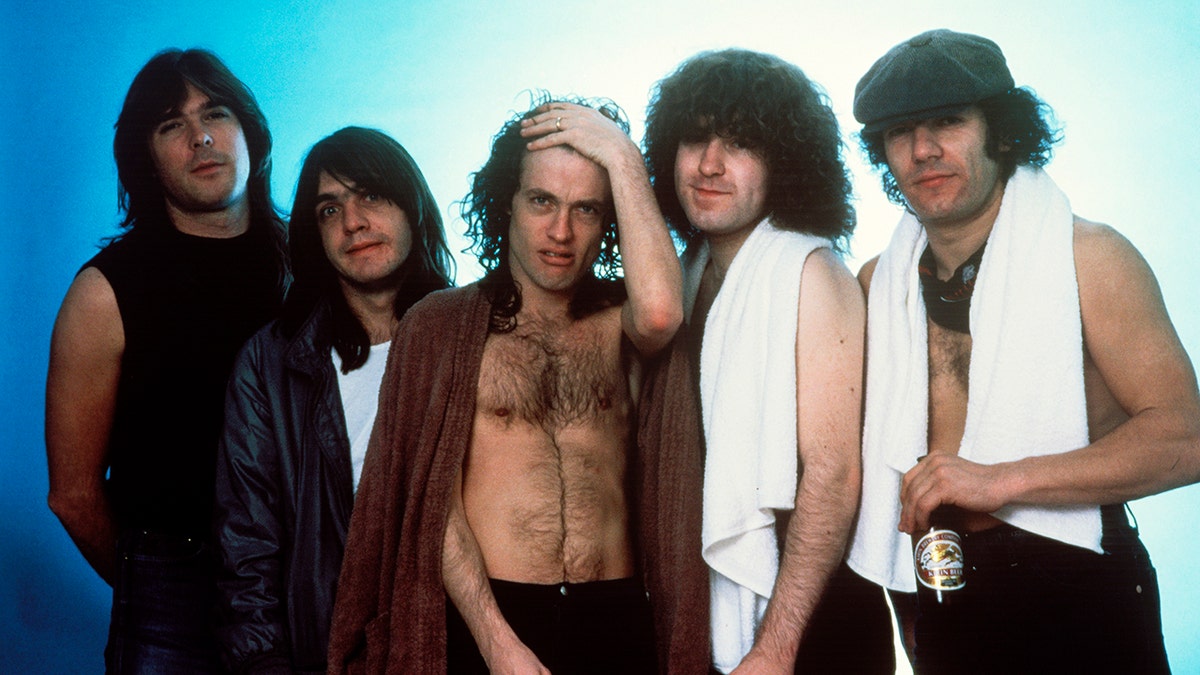 Bassist Cliff Williams, rhythm guitarist Malcolm Young, lead guitarist Angus Young, drummer Simon Wright, and singer Brian Johnson of AC/DC posing backstage