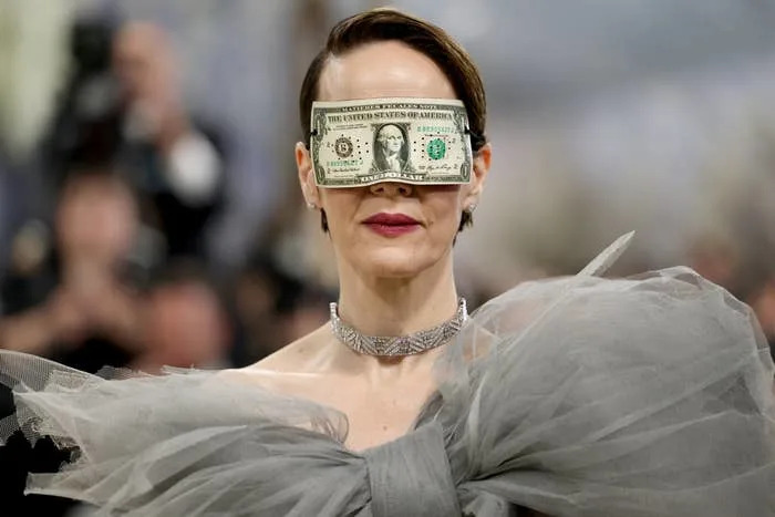 Person on red carpet wearing a dramatic tulle outfit with a dollar bill over their eyes, attending a fashion event