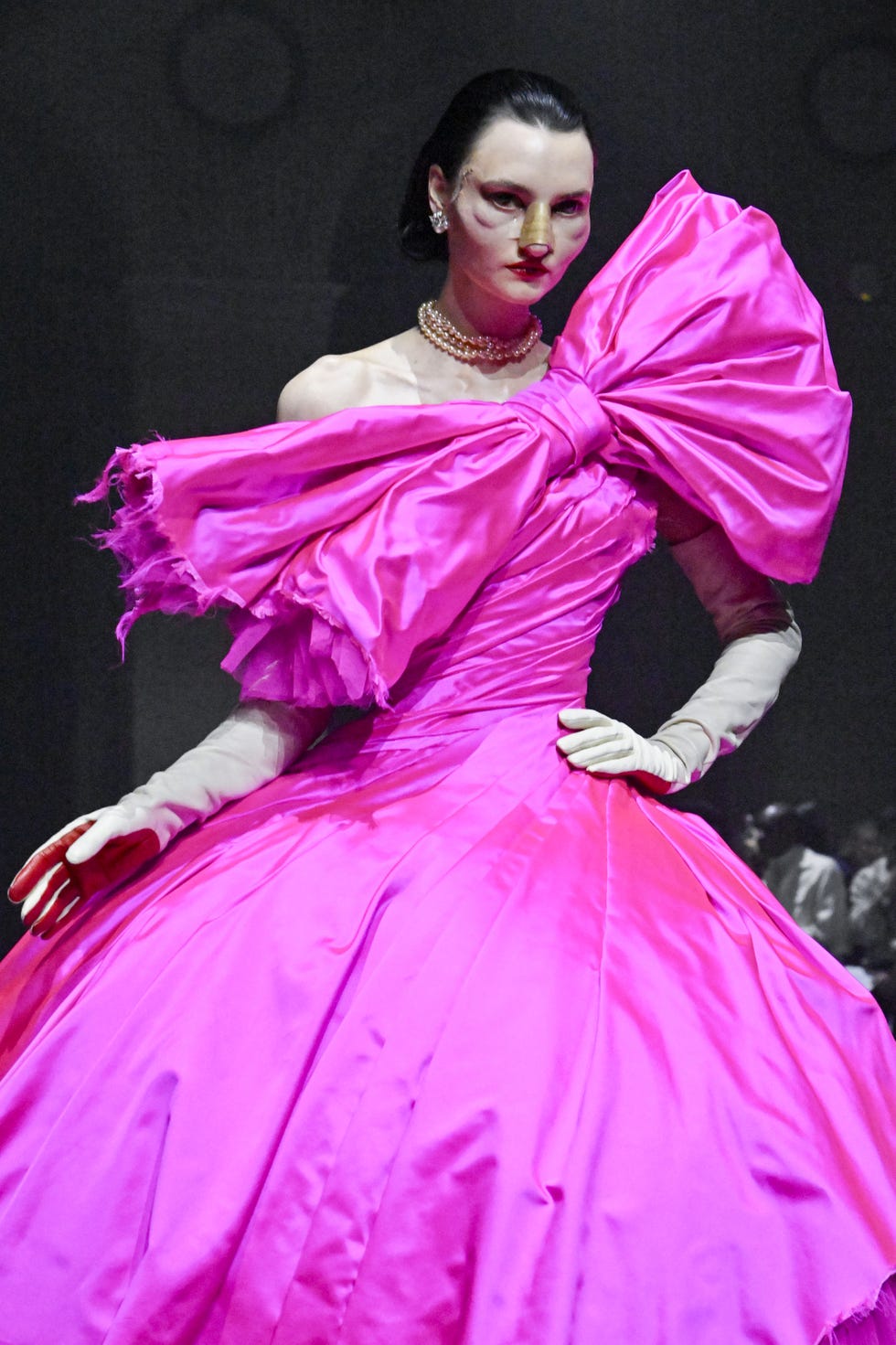Fashion model showcasing a vibrant pink gown with a large bow.