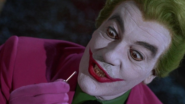 Cesar Romero as the Joker holds up a key and glares at it with wide eyes on the 1966 TV series 