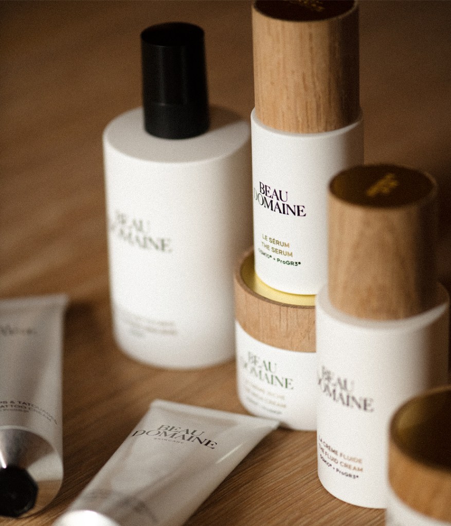 Beau Domaine skincare products including "Le Sérum" and "La Crème Fluide" on a wooden surface.