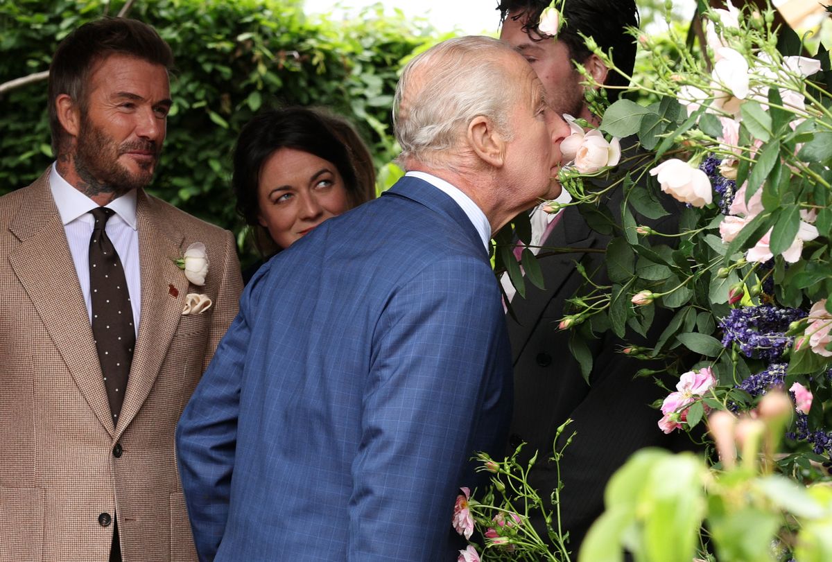 King Charles leaning close to a Sir David Beckham Rose, giving it a whiff