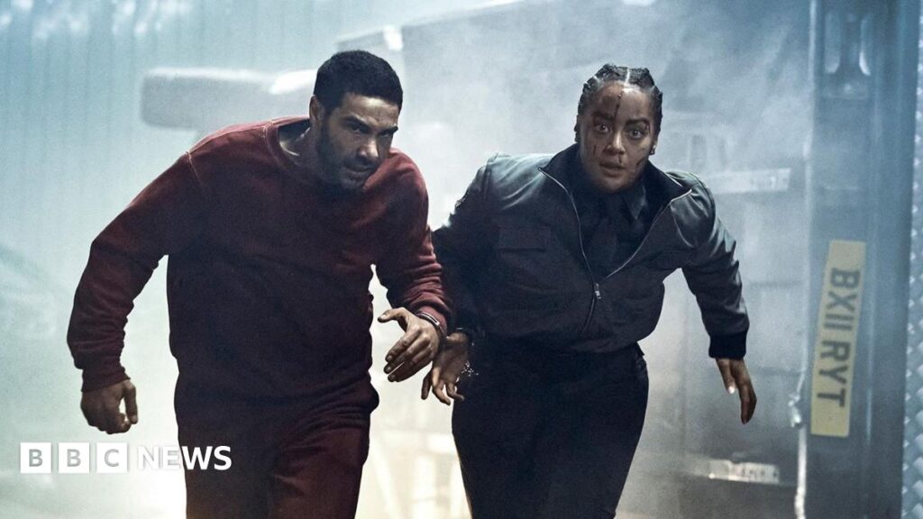 In a scene from the thriller series Prisoner, a prison transport officer and a prisoner run down a tunnel. They are handcuffed to each other and behind them is an overturned van that they were being transported in.